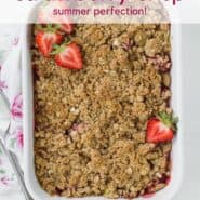 Overhead view of a white baking dish full of cooked strawberries and rhubarb, topped with fresh strawberry halves.