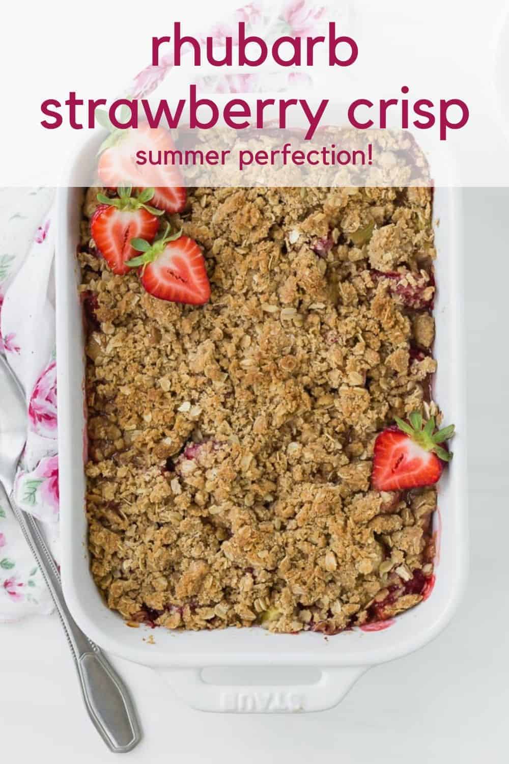 Overhead view of a white baking dish full of cooked strawberries and rhubarb, topped with fresh strawberry halves.