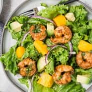 Overhead view of a colorful salad with shrimp, mango and avocado. Text overlay reads, "shrimp, mango, and avocado salad."