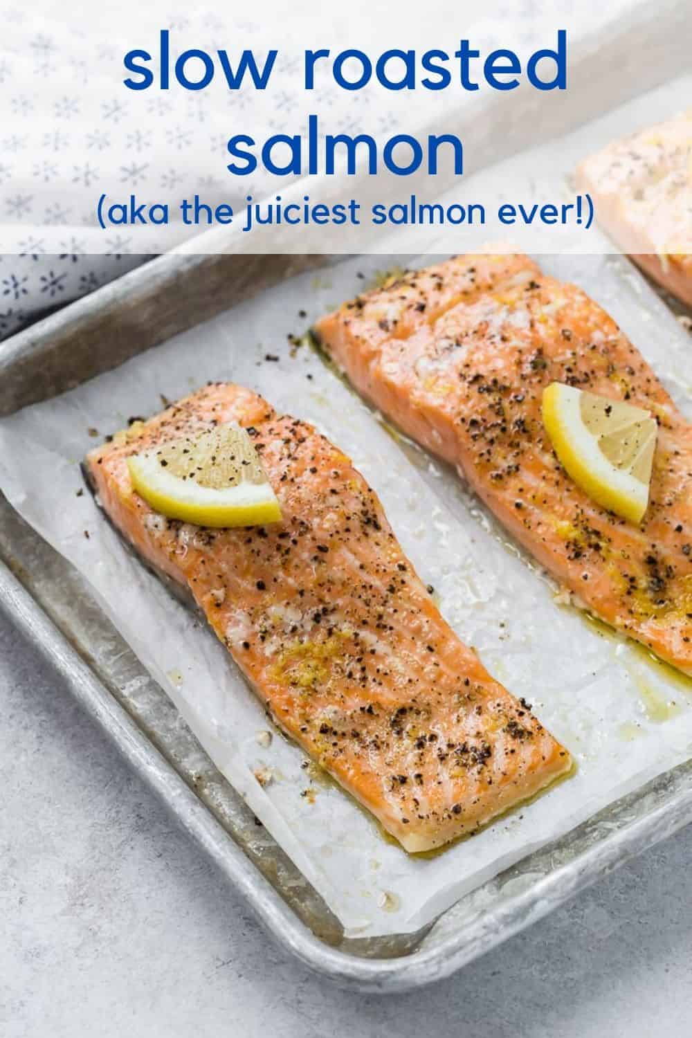 Three salmon fillets on a parchment paper lined sheet pan. Each is topped with pepper and a lemon wedge. Text overlay reads "slow roasted salmon, aka the juiciest salmon ever."