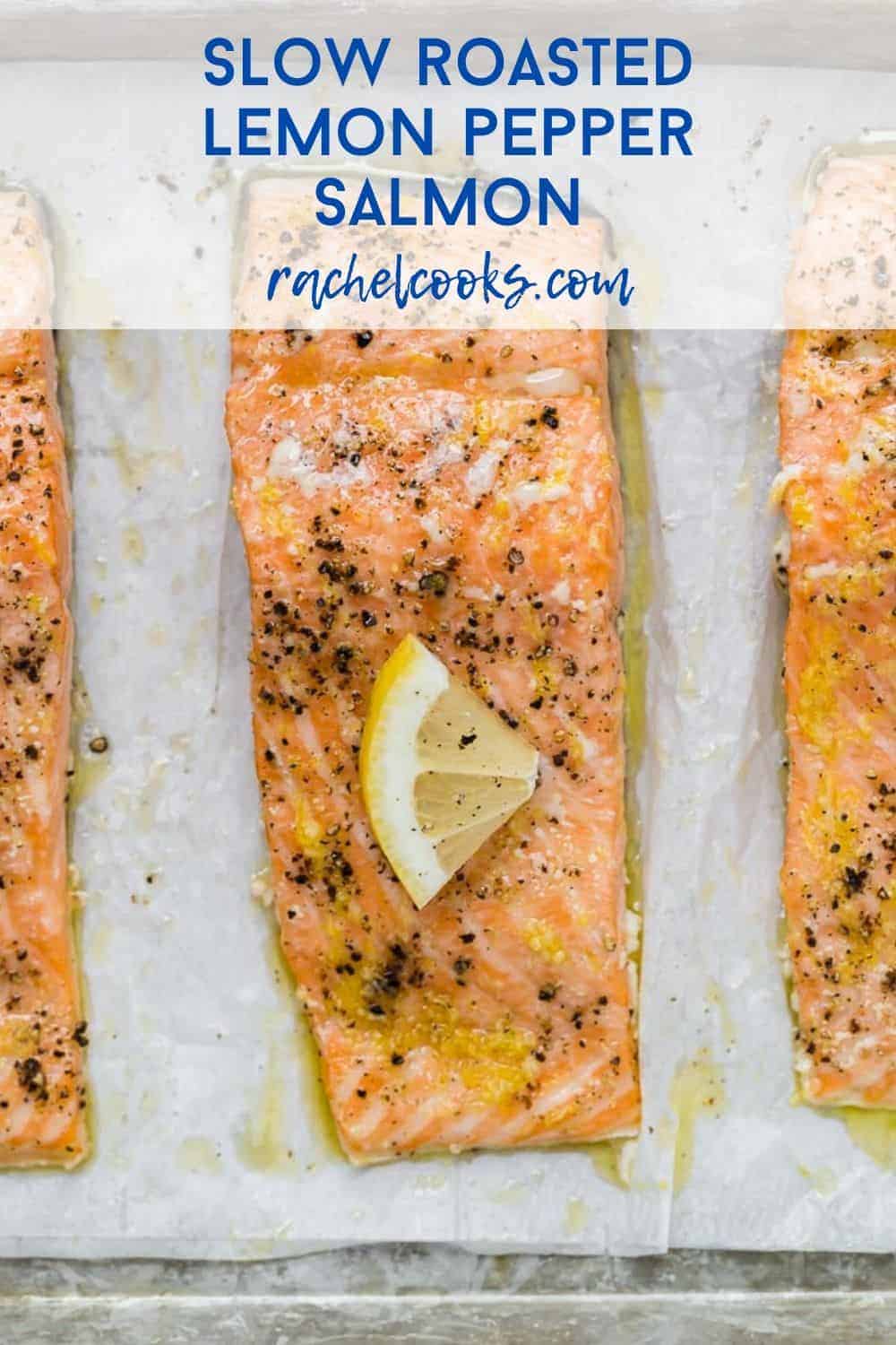 Three salmon fillets on a parchment paper lined sheet pan. Each is topped with pepper and a lemon wedge. Text overlay reads "slow roasted lemon pepper salmon."