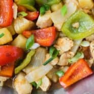 Sweet and sour chicken in a wok, rice and green onions also pictured.