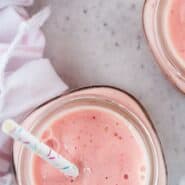 Overhead view of a pink fruit smoothie with fun sprinkles straws.