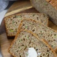 Overhead view of sliced zucchini bread, with a dab of butter on it. A text overlay reads "whole wheat zucchini bread."