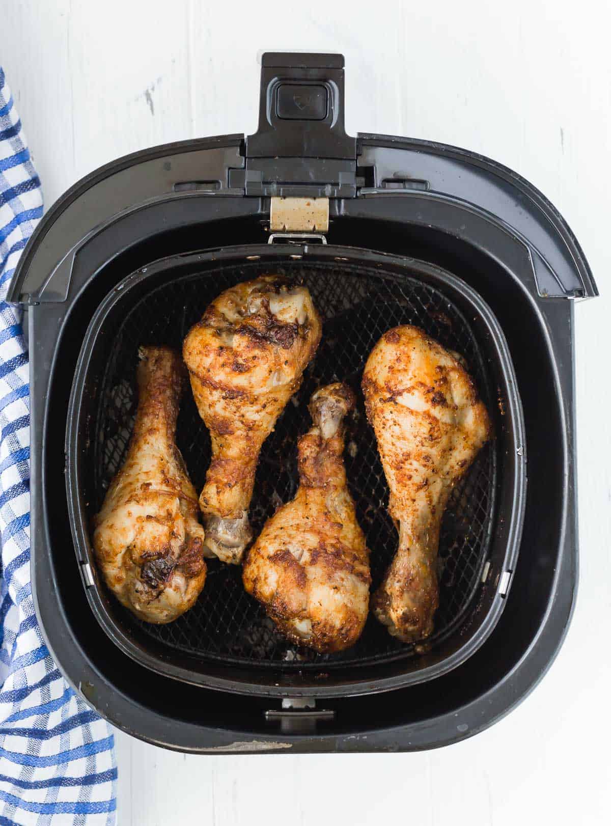 Overhead view of four chicken drumsticks in the basket of an air fryer.