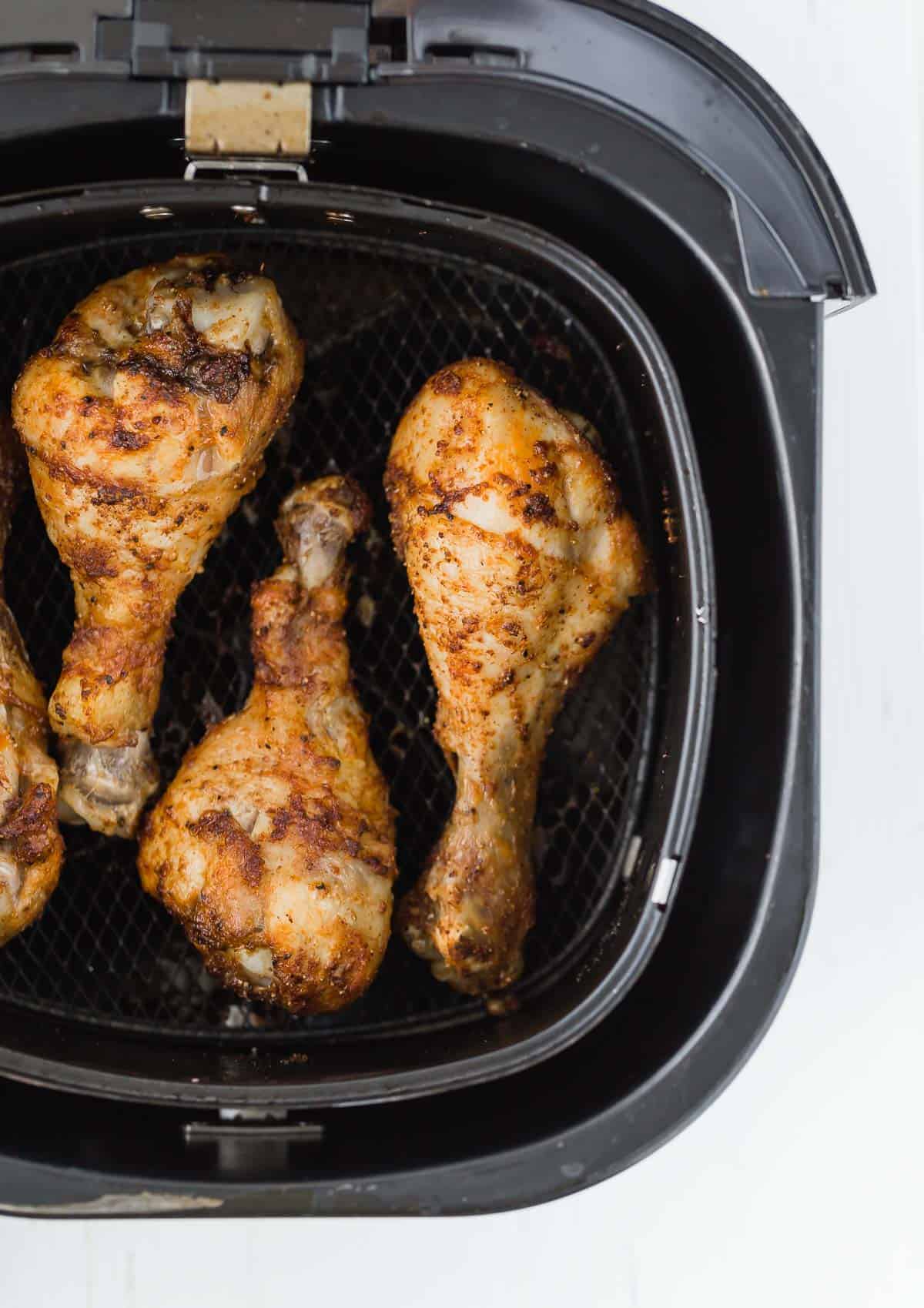 Overhead view of a black air fryer basket with cooked chicken drumsticks inside it.