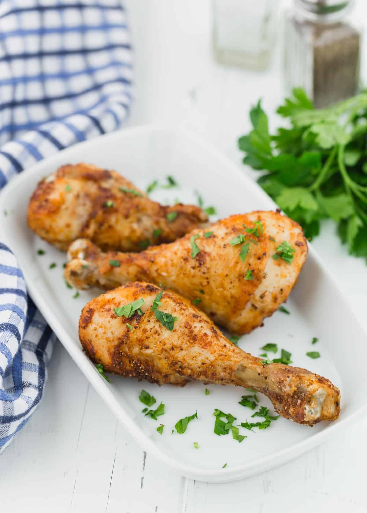 Three cooked drumsticks on a white serving plater, on a white wooden background.