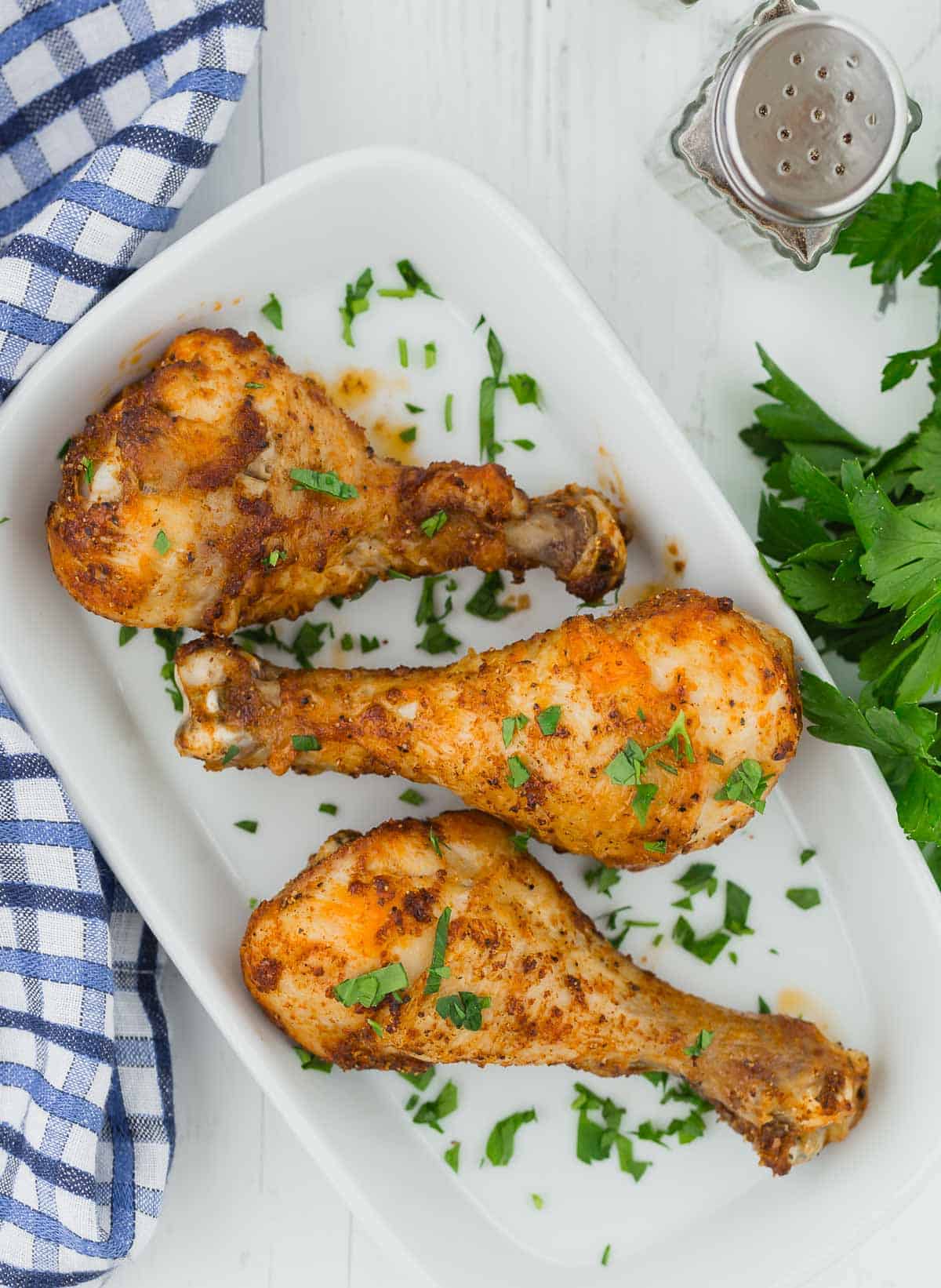 Overhead view of three seasoned chicken drumsticks on a white platter.