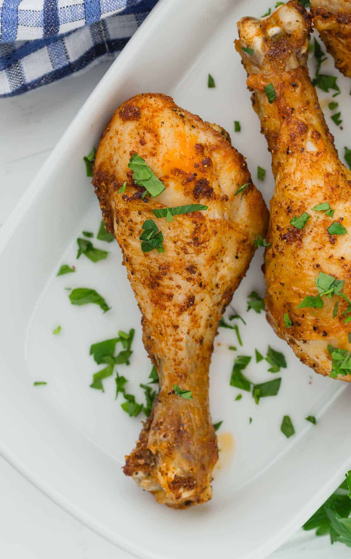 Overhead view of a chicken drumstick on a white plate, sprinkled with fresh parsley.