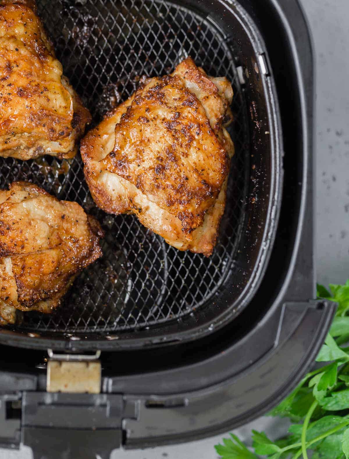 Overhead view of three chicken thighs in an air fryer basket.