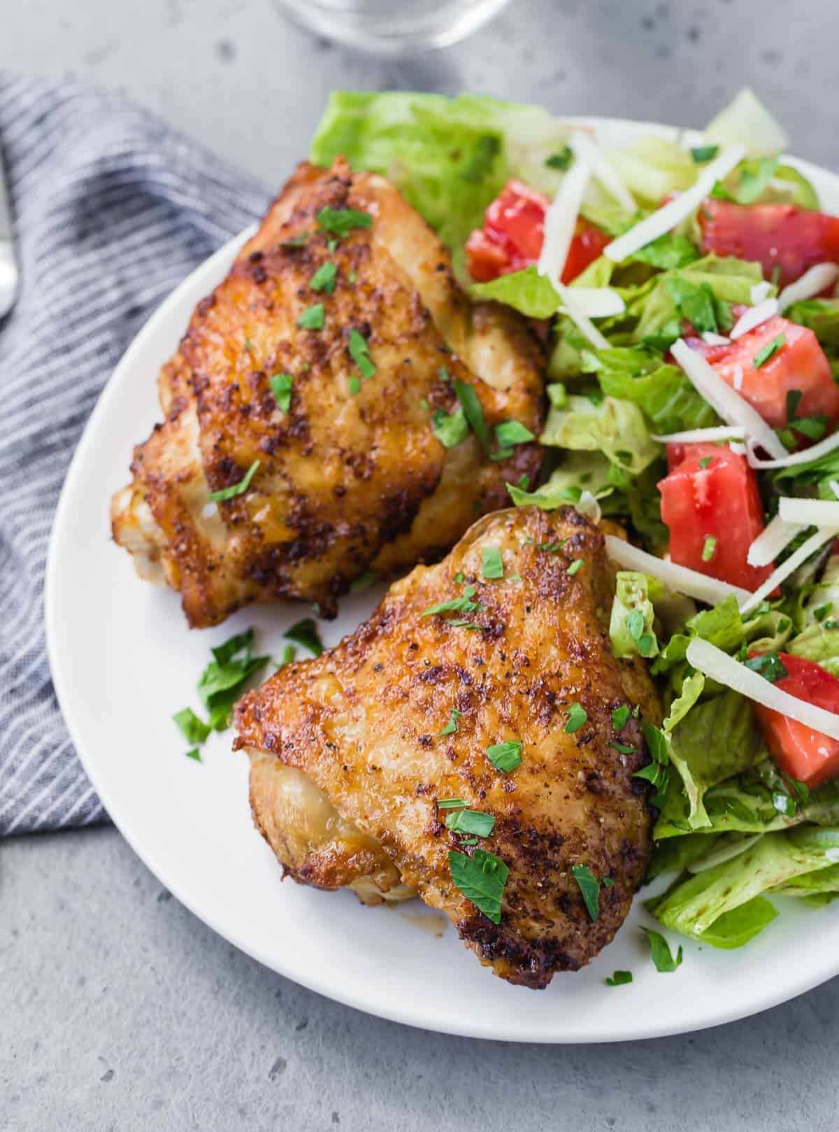 Overhead view of two chicken thighs on a plate with a tossed salad.