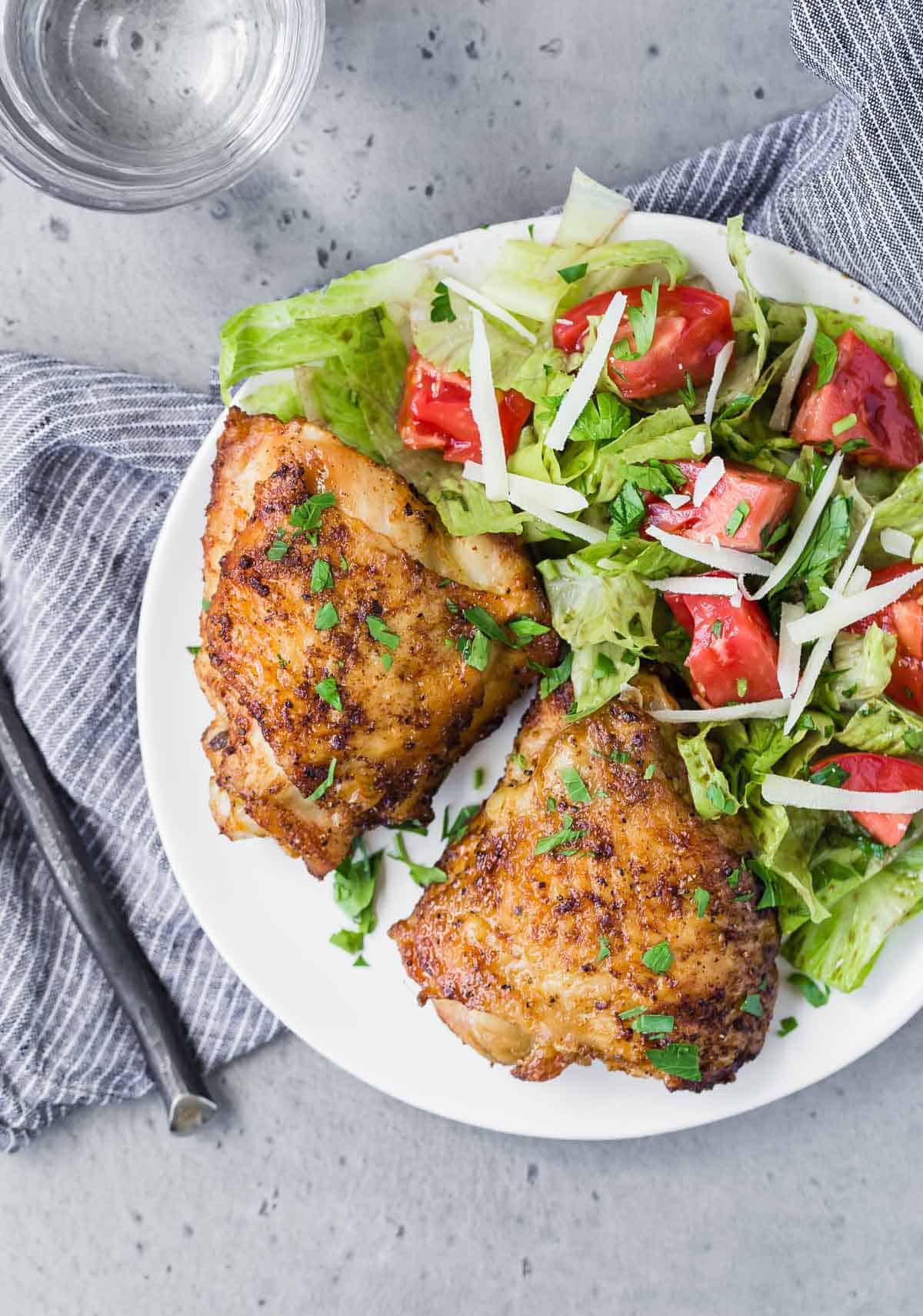 Overhead view of two chicken thighs on a plate with a tossed salad.