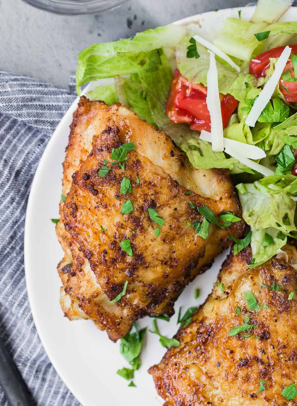 Overhead view of two chicken thighs on a plate with a tossed salad.