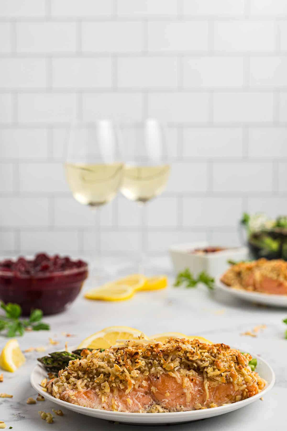 Cooked salmon served on a white plate with white wine and additional food in the background.