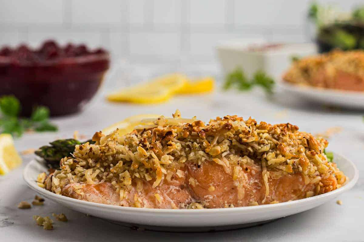 Close up of cooked salmon on a plate.. Salmon is crusted with almonds and parmesan cheese.