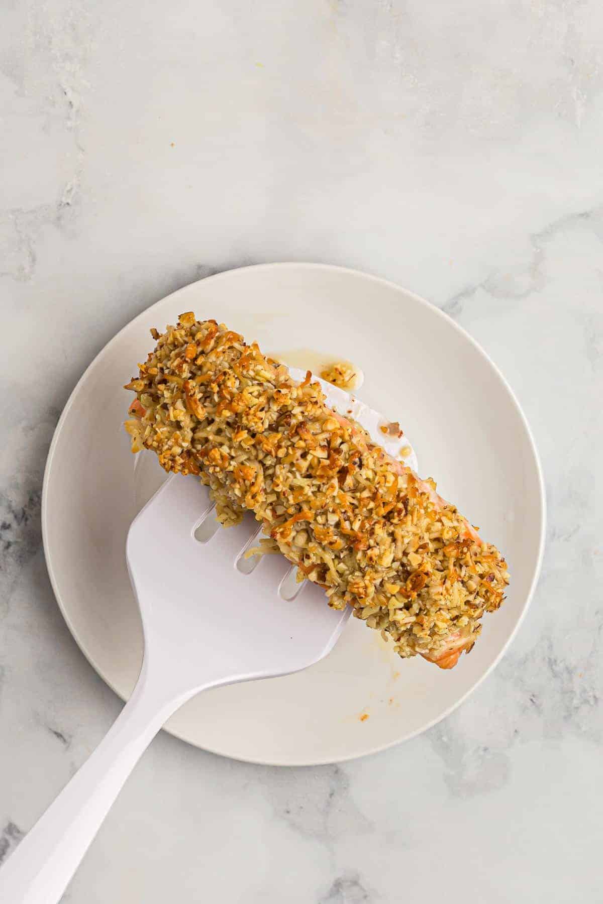 Cooked salmon on a spatula on a white marble background, over a white plate.