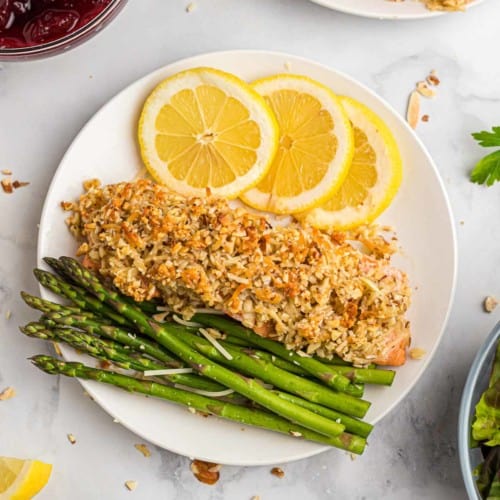 Overhead view of almond and parmesan crusted salmon on a plate with lemon slices and asparaugs.