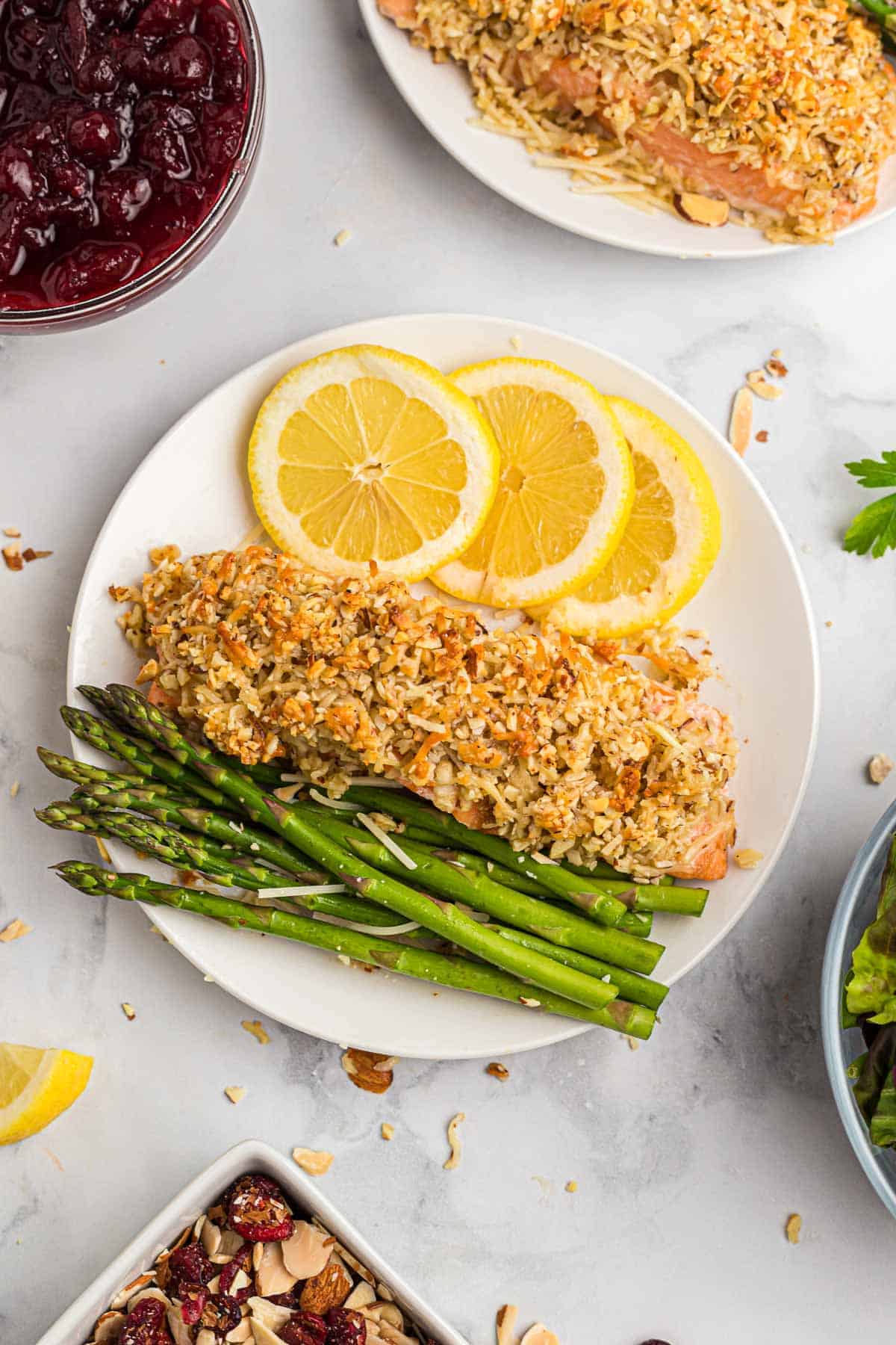 Overhead view of almond and parmesan crusted salmon on a plate with lemon slices and asparaugs.