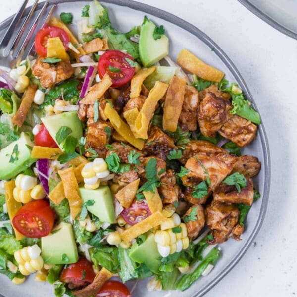 Overhead view of a colorful chopped salad on a grey plate. Salad includes bbq grilled chicken, lettuce, onion, tomato, crispy tortilla strips, avocado, corn and more!