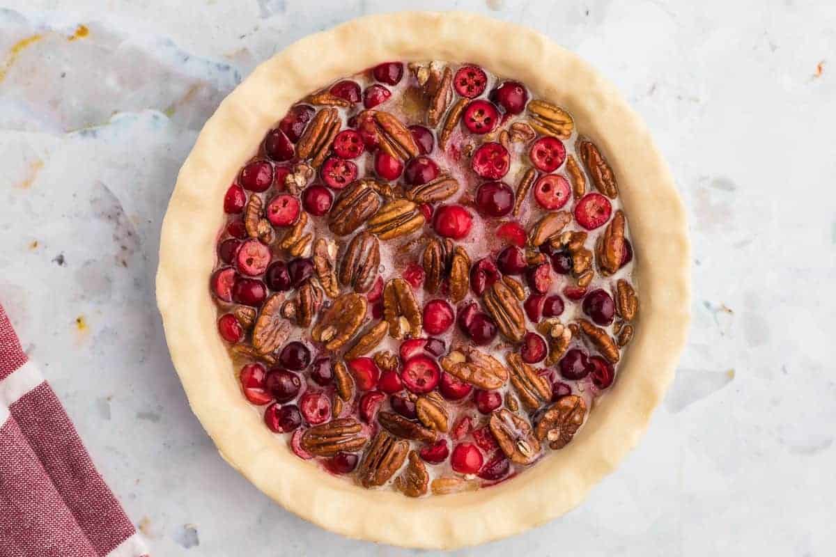 Unbaked pecan pie with cranberries, overhead view.