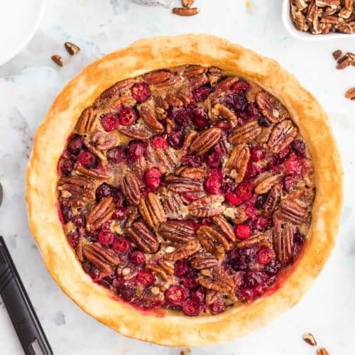 Overhead view of pecan pie with cranberries, surrounded by individual ingredients.
