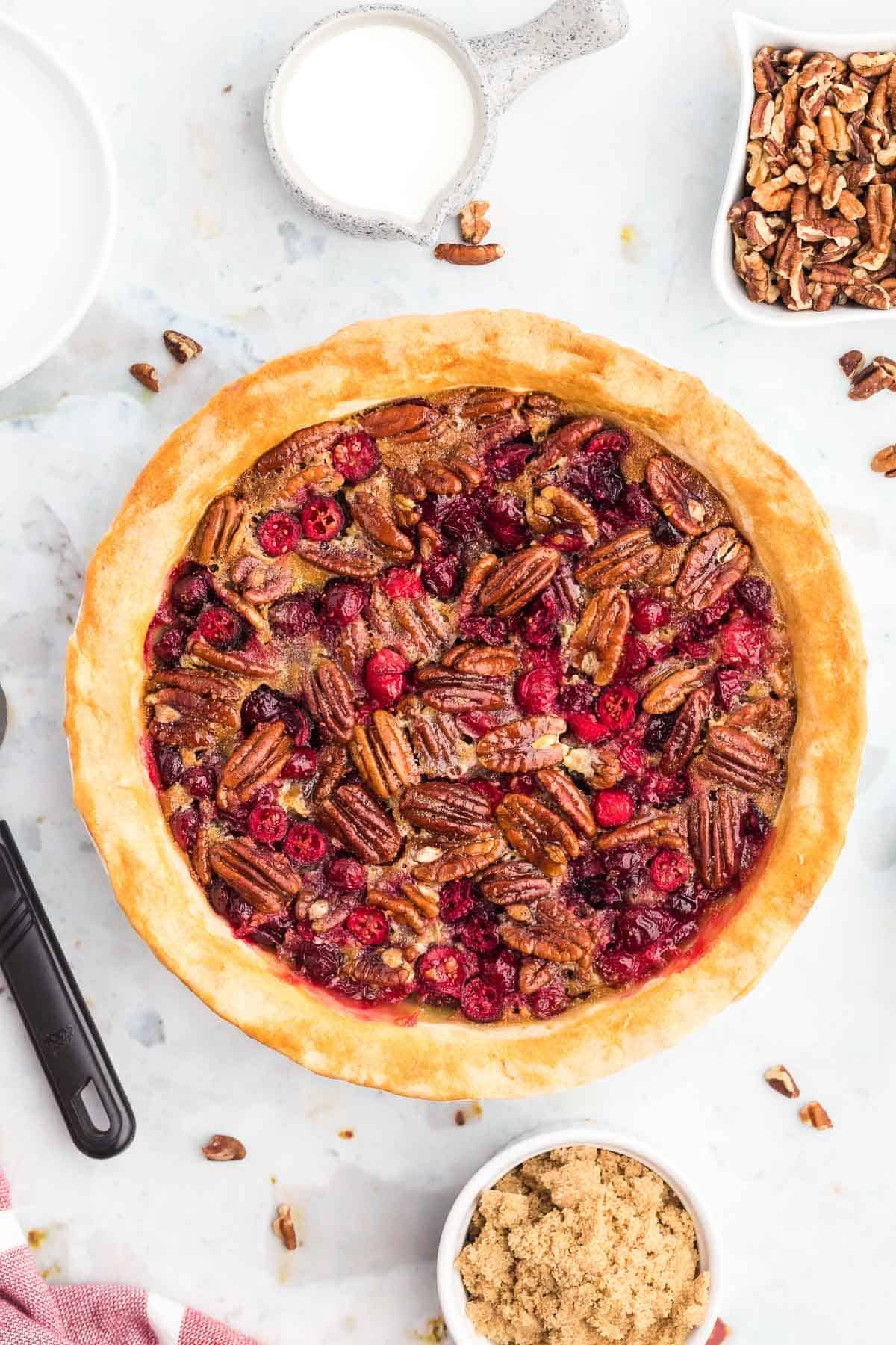 Overhead view of pecan pie with cranberries, surrounded by individual ingredients.