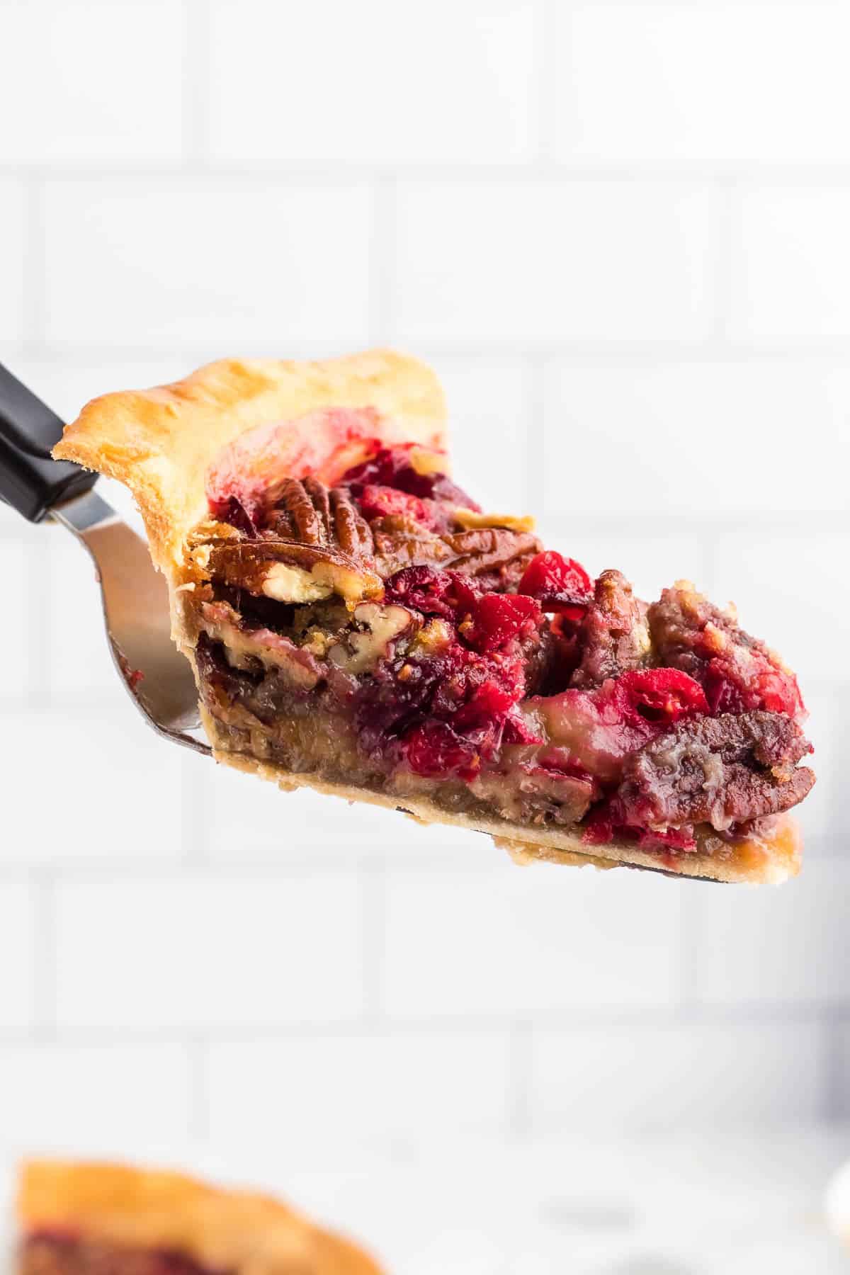 Slice of pie with pecans and cranberries on a spatula.