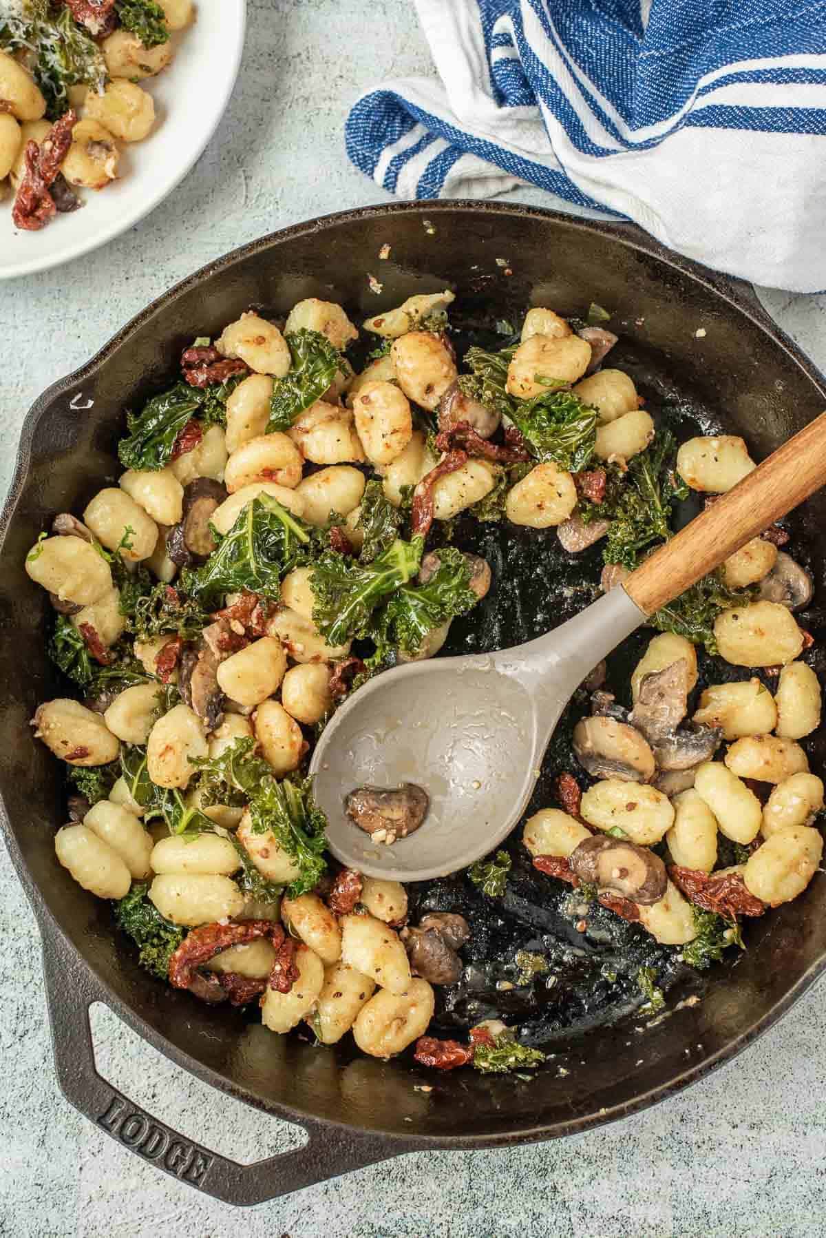 Black skillet half full of gnocchi, depicting it being served out of skillet.