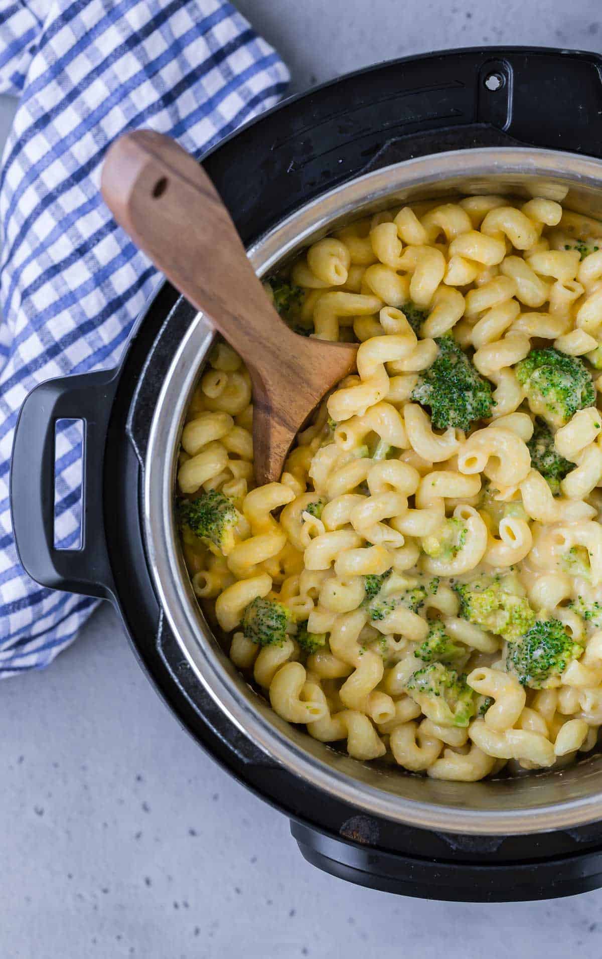 Overhead view of an instant pot pressure cooker filled with macaroni and cheese with broccoli. Wooden spoon also visible.