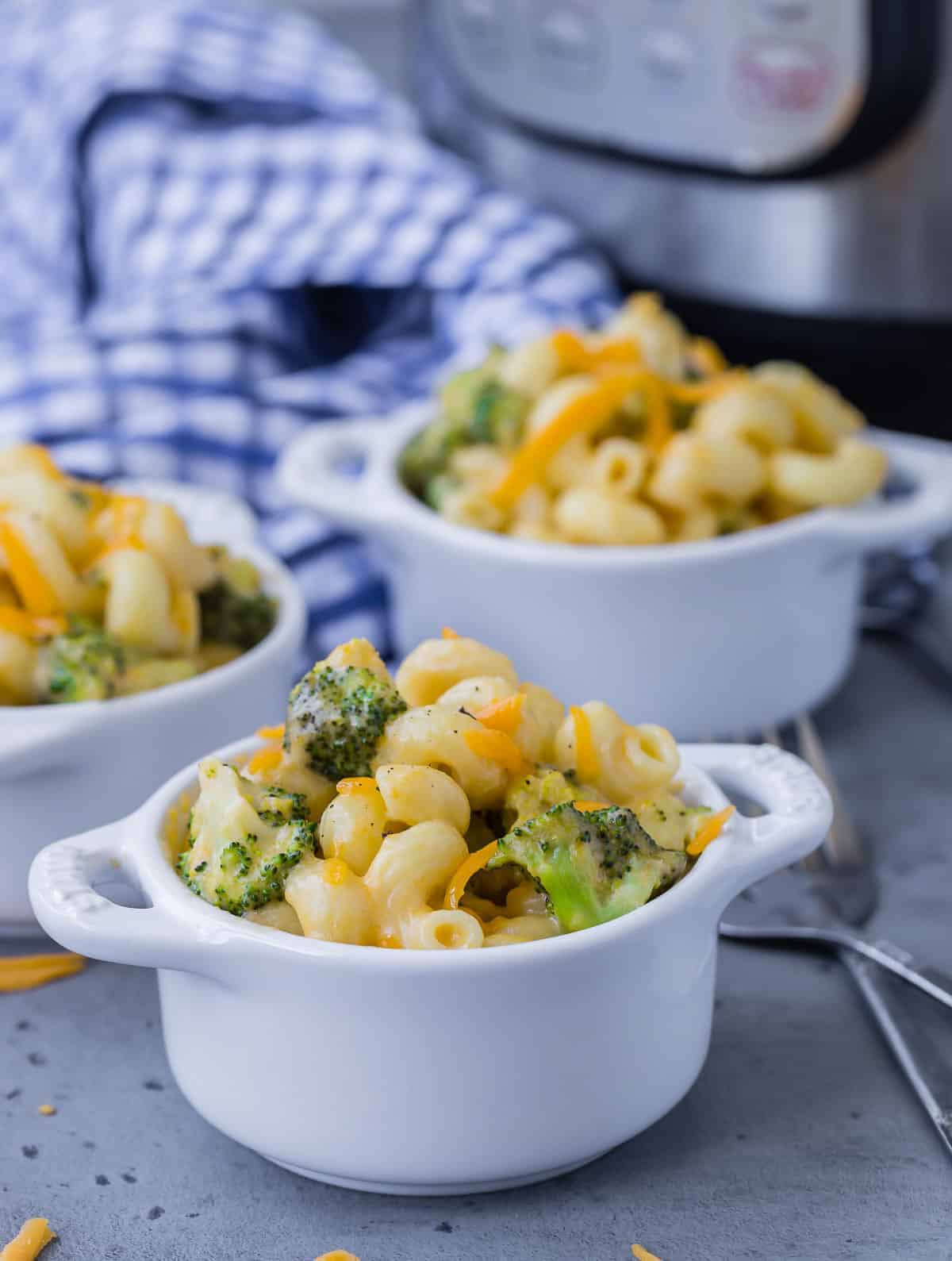 Three small white bowls filled with broccoli mac and cheese, with an instant pot in the background.