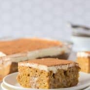 Pumpkin poke cake on a plate, with additional cake in the background. Text overlay reads "the best pumpkin poke cake - rachelcooks.com"