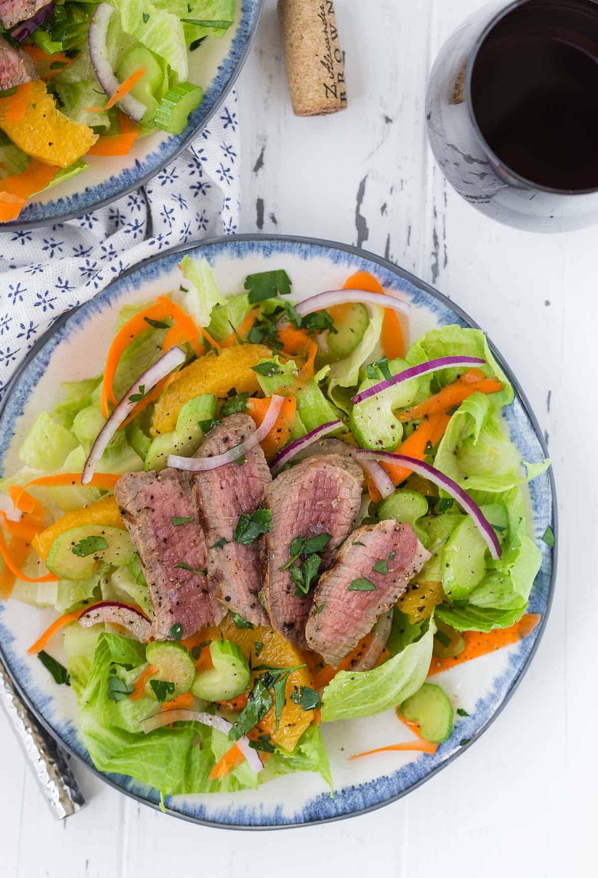 Overhead view of a green leaf lettuce salad topped with steak, oranges, and onion.