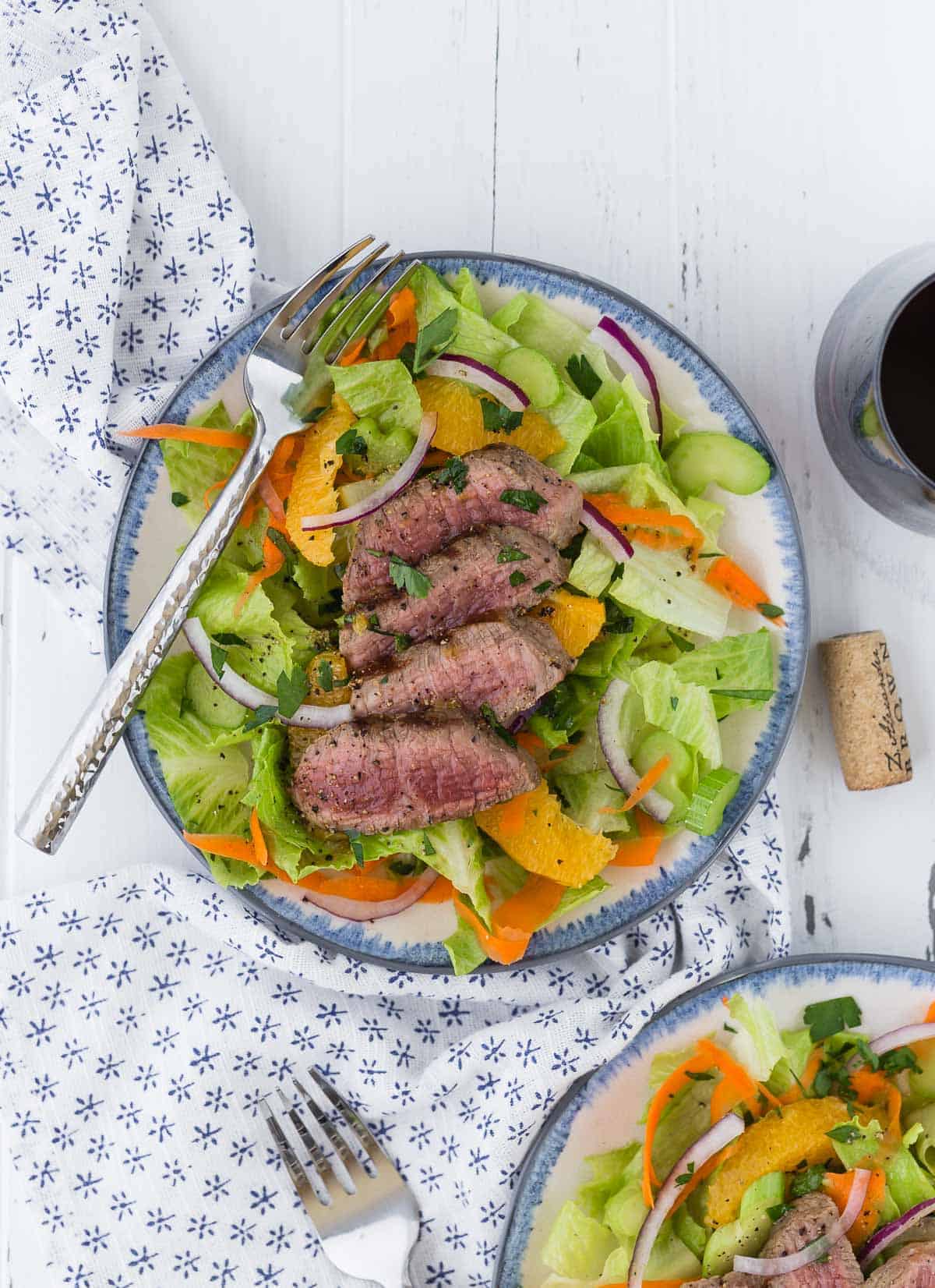 Overhead view of a green leaf lettuce salad topped with steak, oranges, and onion.