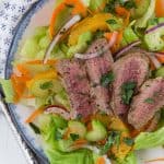 Overhead view of a green leaf lettuce salad topped with steak, oranges, and onion.