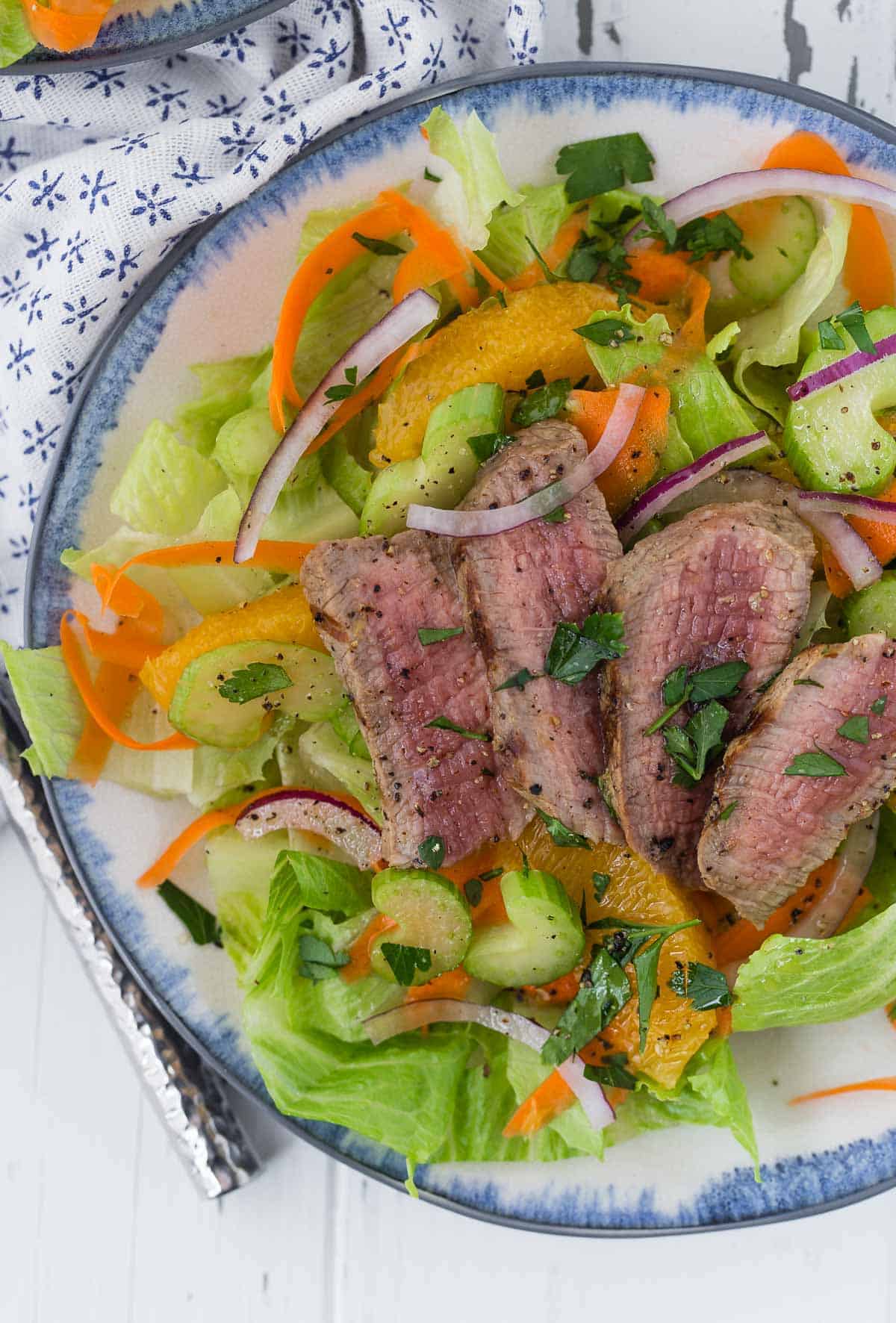 Overhead view of a green leaf lettuce salad topped with steak, oranges, and onion.