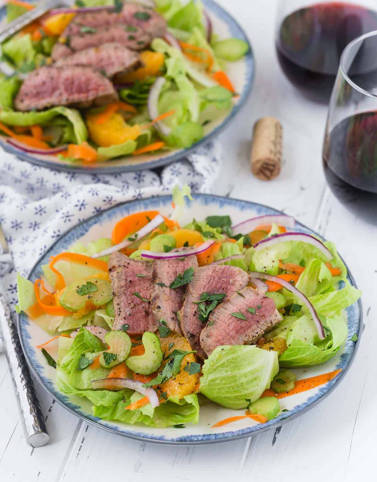 Green leaf lettuce salad topped with steak, oranges, and onion.