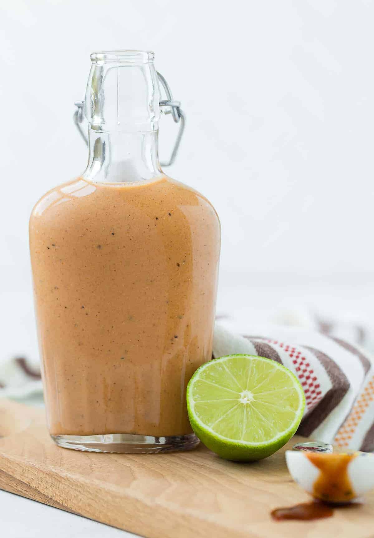 Glass bottle full of light orange salad dressing. A half a lime is in the foreground.