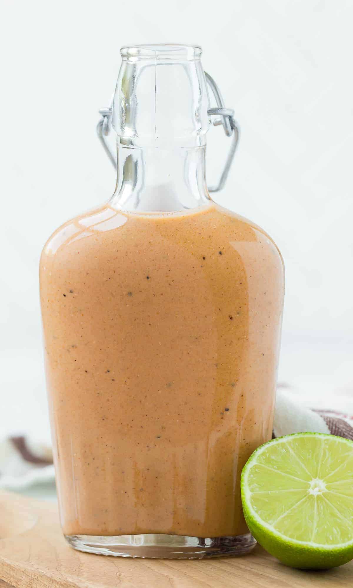 Glass bottle full of light orange salad dressing. A half a lime is in the foreground.