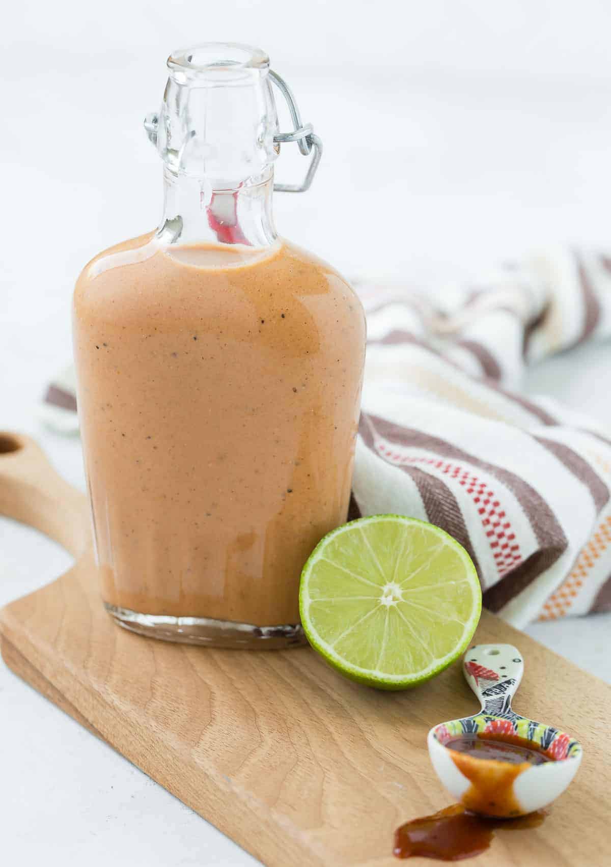 Small glass bottle of sweet bbq salad dressing on a wooden cutting board.