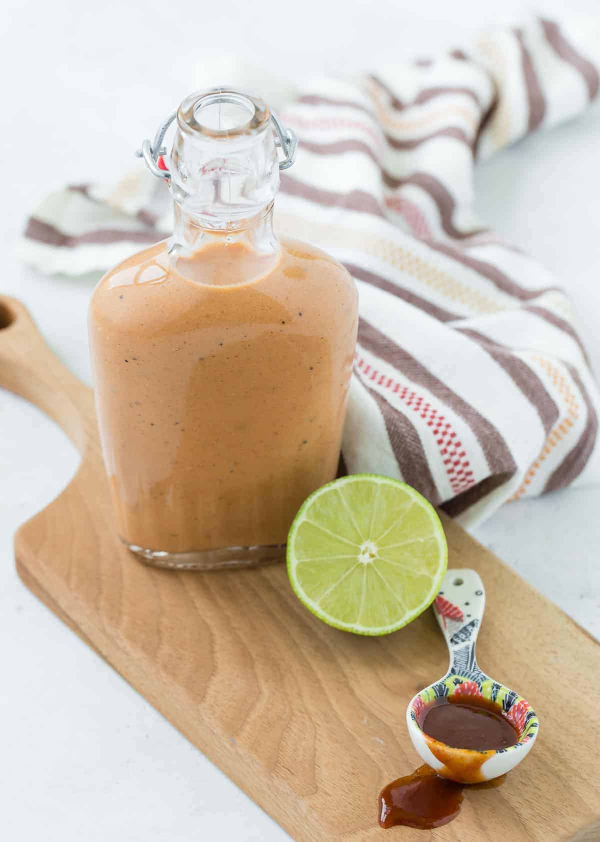 Glass bottle full of light orange salad dressing. A half a lime is in the foreground.