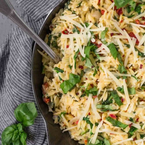 Overhead view of vegetarian orzo in a cast iron skillet, topped with fresh basil and parmesan cheese.