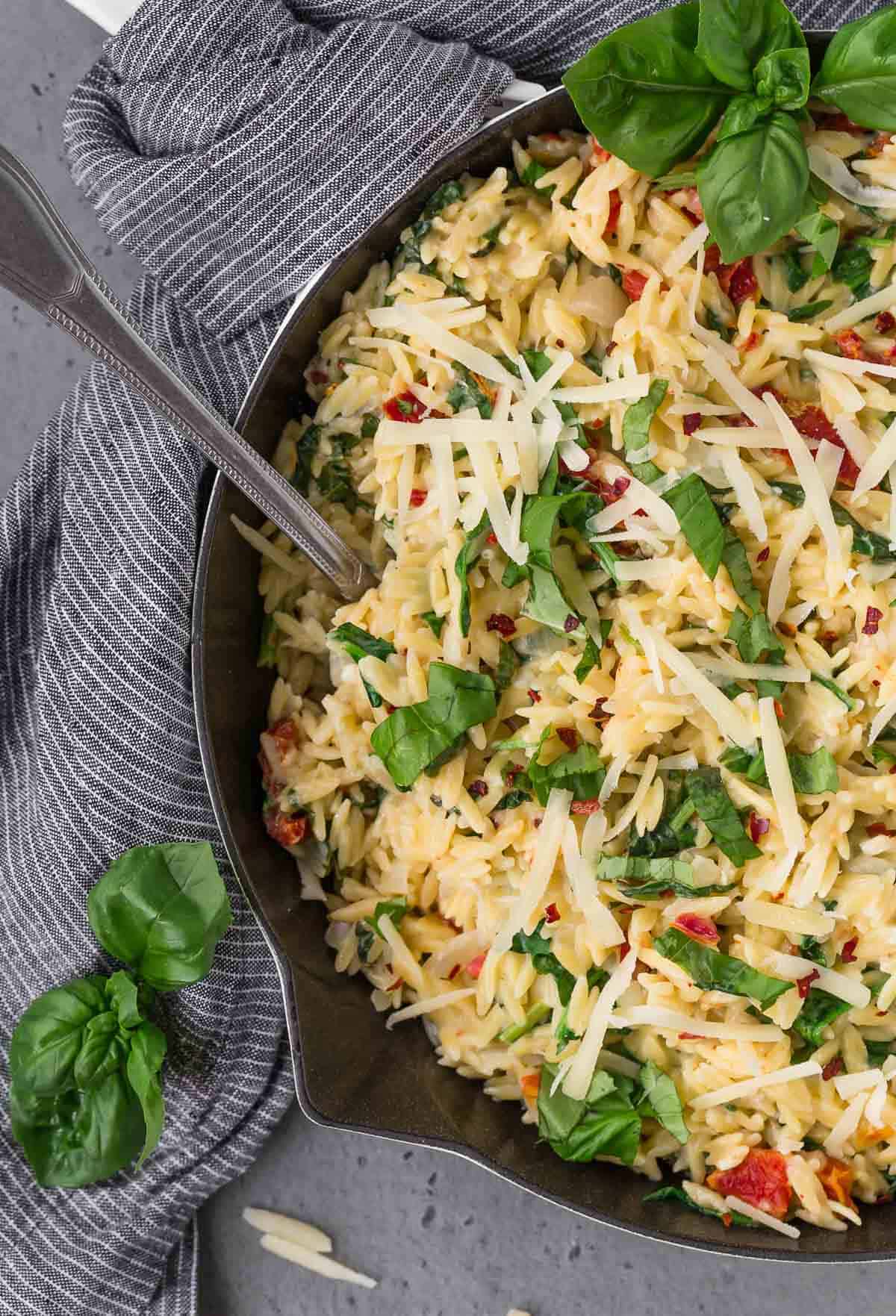 Overhead view of vegetarian orzo in a cast iron skillet, topped with fresh basil and parmesan cheese. 