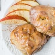 Apple fritters with glaze on a plate with sliced apples.