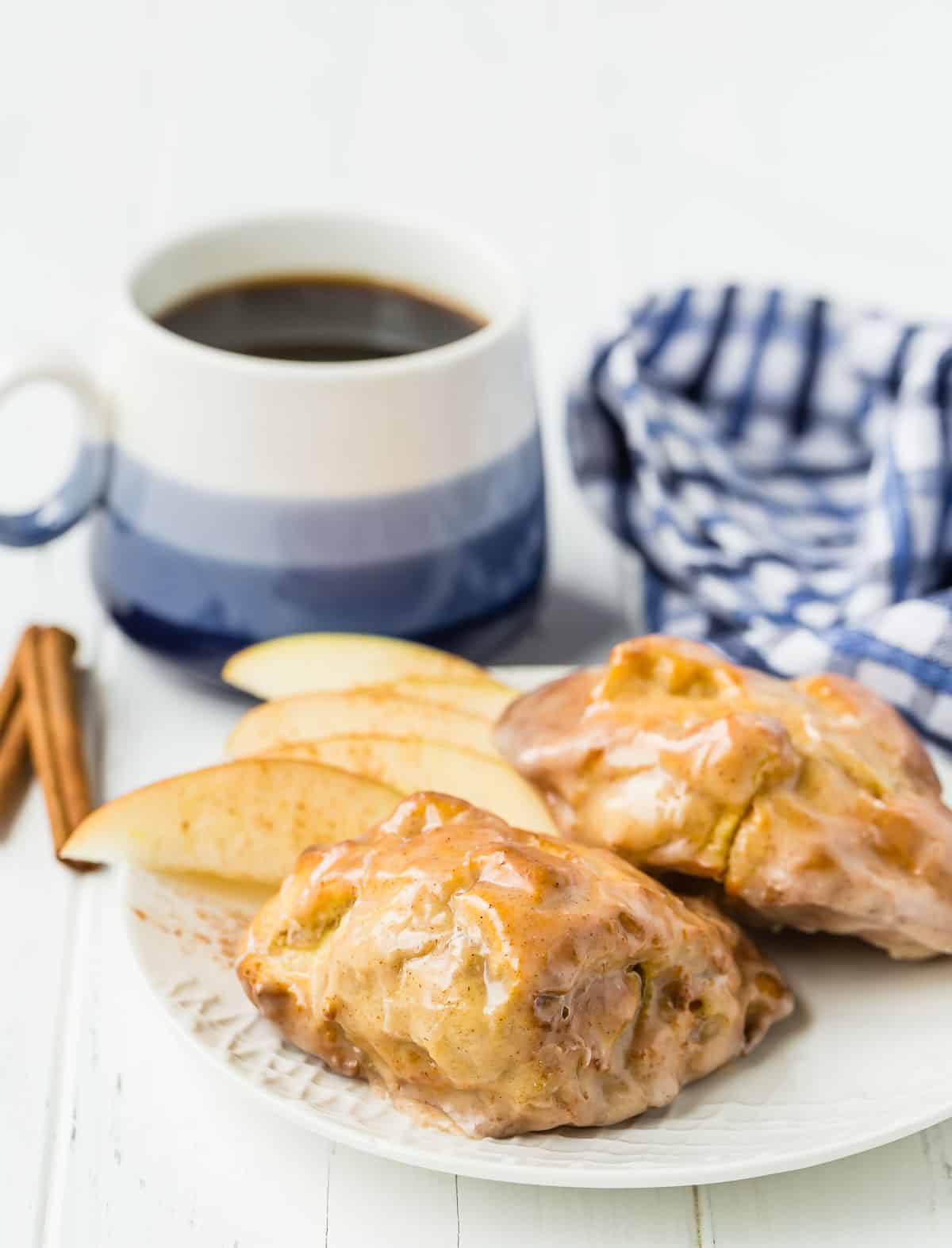 Apple fritters on a white plate with a blue and white cup of coffee in the background.