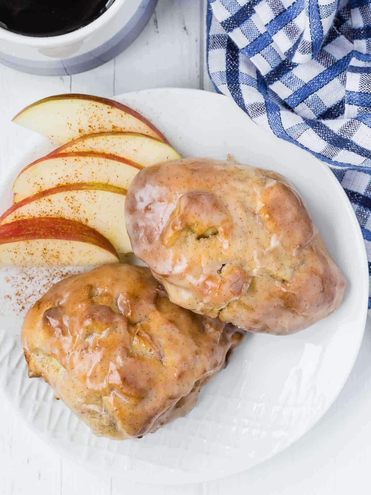 Two air fried apple fritters on a plate with sliced apples, coffee also visible.