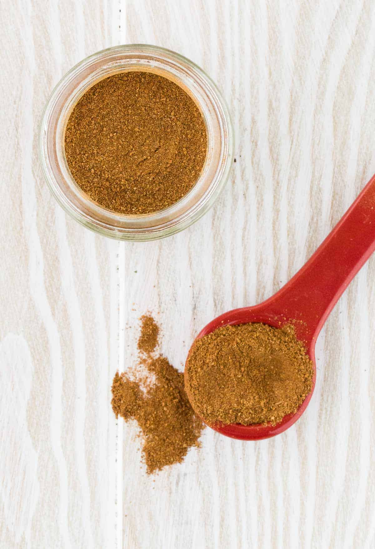 Apple pie spice mixture on a spoon, and in a jar on a white wooden background.