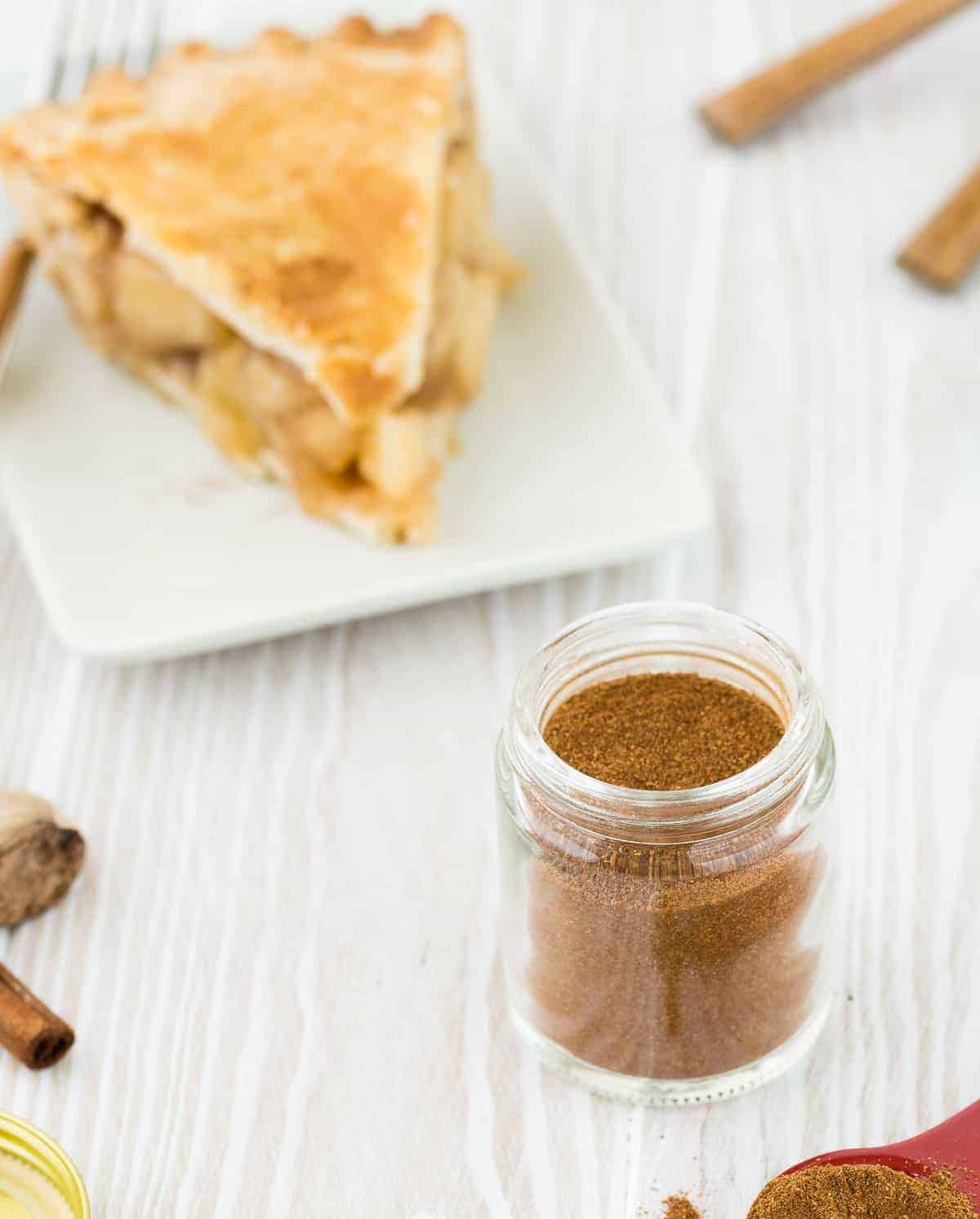 Apple pie on a white plate, with apple pie spices in the foreground.