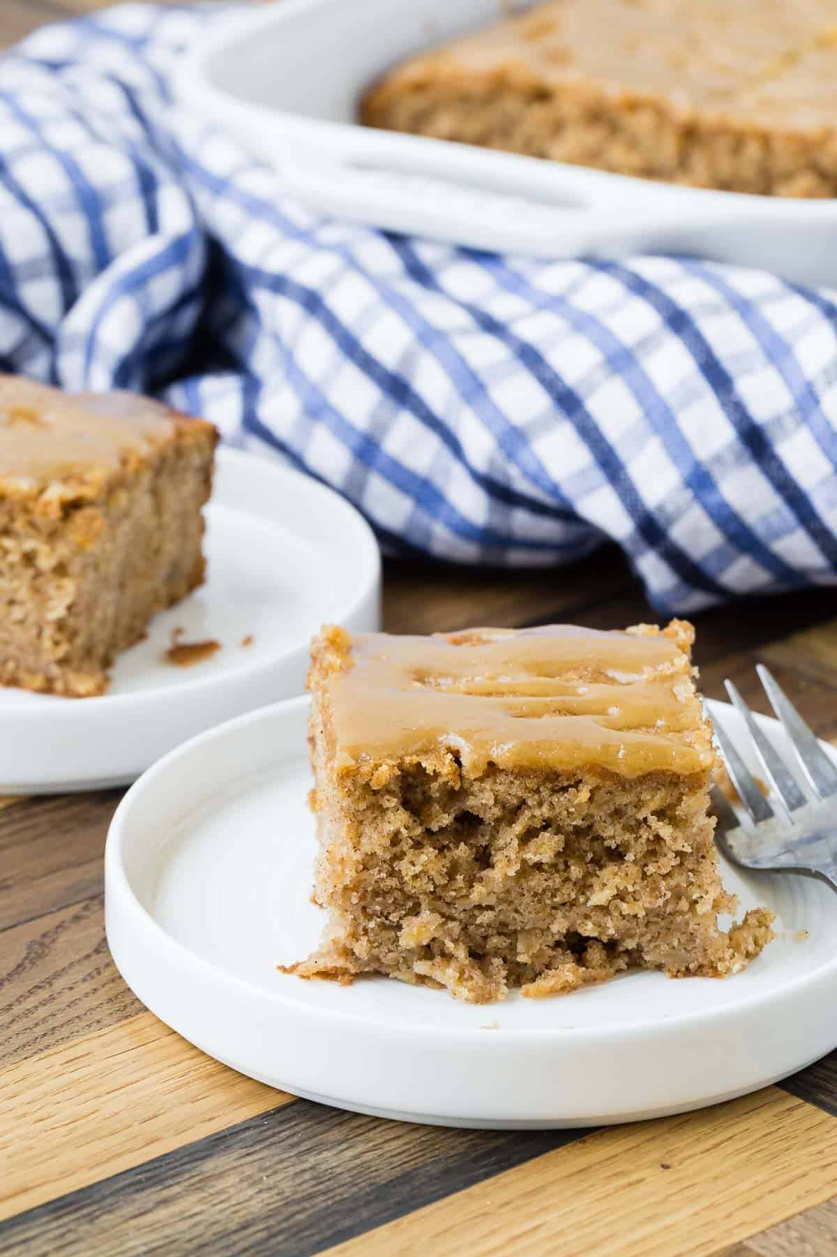Slice of spiced apple cake on a white plate, more cake in background.