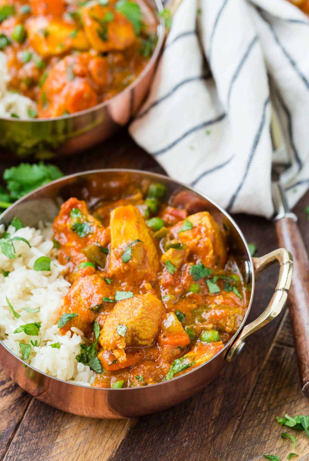 Chicken tikka masala in a small copper pot with rice and cilantro.