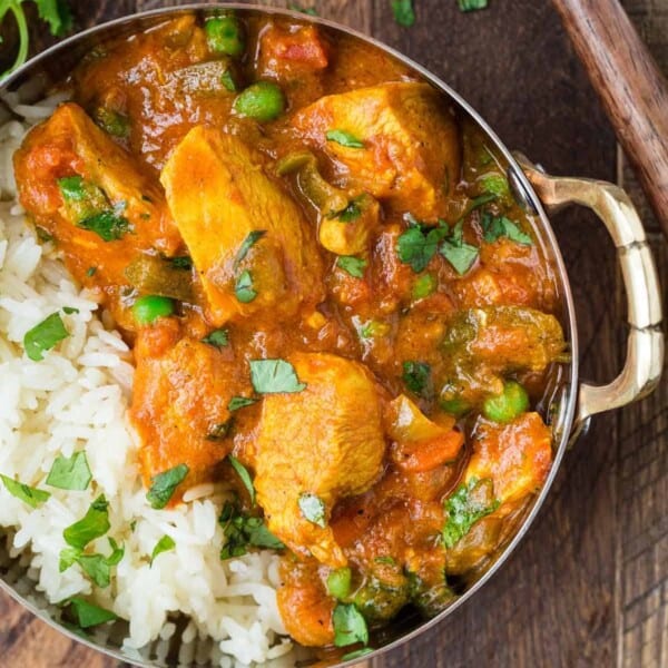 Close up of chicken served with rice, carrots, and a creamy tomato sauce. It is served in a small bowl with rice and cilantro.